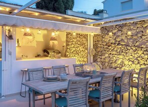 Un área de comedor al aire libre con un muro de piedra de fondo, una mesa de madera y sillas.