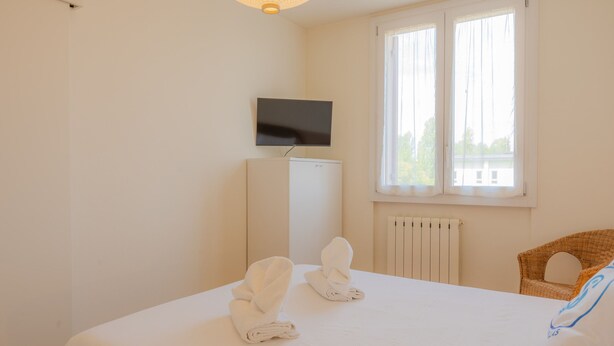Quarto de hotel com cama, televisão na parede, radiador e janela com cortinas.