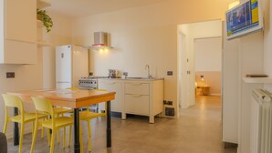 Cozinha moderna com armários brancos, fogão e pia. Há uma mesa de jantar com cadeiras amarelas.