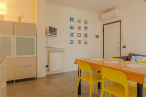 A room with a dining table, chairs, a radiator, a TV, and a door. - SG Family - Il Meriggio (Peschiera del Garda)