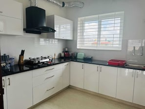 A modern kitchen with white cabinets, a black countertop, and a window with blinds.