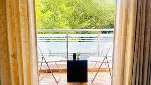 Uma varanda com mesa e cadeiras, um vaso de planta e vista para o verde.
