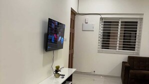 Sala de estar con televisor de pantalla plana montado en la pared, mueble de madera para entretenimiento, sofá marrón y una ventana con persianas.