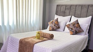 Ein ordentlich bezogenes Bett mit weißer Bettdecke, zwei gemusterten Kissen und einer braunen Tagesdecke.