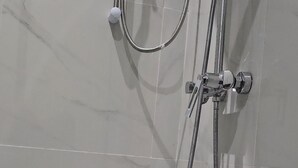 Ein Duschbereich mit gefliesten Wänden und Boden, einer Handbrause und einer an der Wand montierten Armatur.