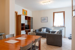 A living room with a wooden dining table, grey sofa, and a television on a wooden cabinet. - SG Family - Park Everywhere Apartment (Castelnuovo del Garda)