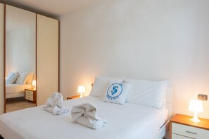 A hotel room with a bed, two bedside tables, a nightstand, a mirror, and a wall-mounted light fixture. - SG Family - Park Everywhere Apartment (Castelnuovo del Garda)