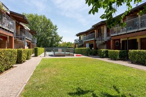 A residential area with a paved walkway, a small grassy area, and two multi-story buildings with balconies. - SG Family - Park Everywhere Apartment (Castelnuovo del Garda)