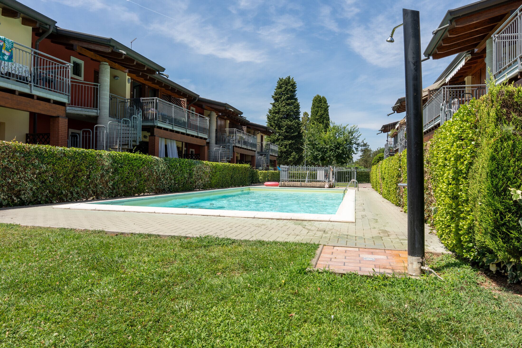 A swimming pool surrounded by a well-maintained lawn and hedges, with multi-story buildings in the background.
