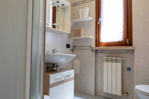 A bathroom with a white sink, wooden vanity, a toilet, and a window with a wooden frame. - SG Family - Park Everywhere Apartment (Castelnuovo del Garda)