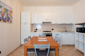 Eine kleine Küche mit weißen Schränken, einem Holztisch und blauen Stühlen.