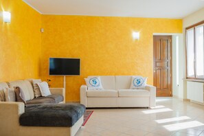 A living room with a sofa set, a flat-screen TV, and a wooden door. - SG Family - Casa Bertolini (Castelnuovo del Garda)