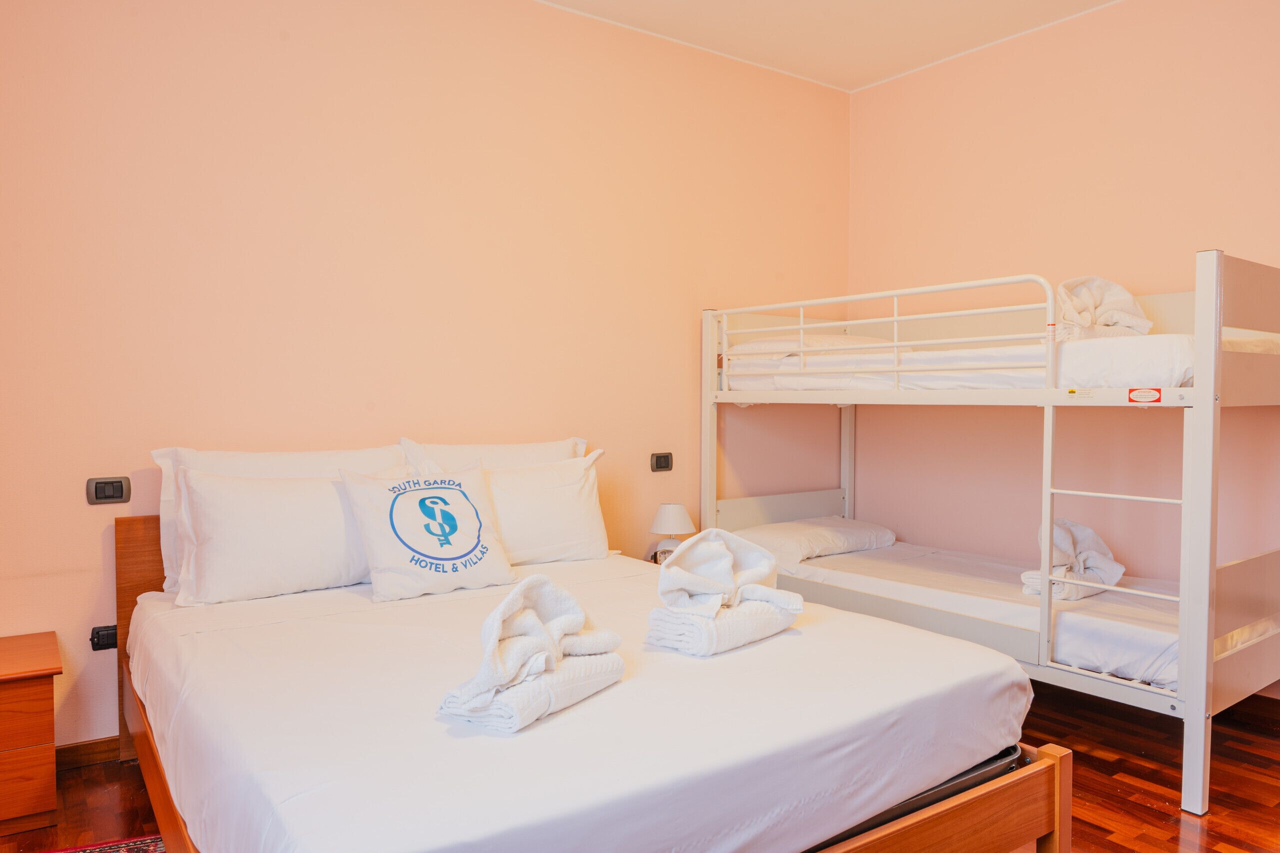 Ein Hotelzimmer mit Etagenbett, einem Einzelbett und einem Nachttisch aus Holz.