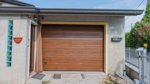 Puerta de garaje residencial con un muro de concreto, una cerca metálica y un pequeño jardín.