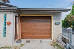 A residential garage door with a concrete wall, a metal fence, and a small garden area. - SG Family - Casa Bertolini (Castelnuovo del Garda)
