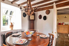 A dining area with a wooden table set for four, a vintage clock, and a rustic chandelier. - Holiday Home Near Dolgellau (Dolgellau)