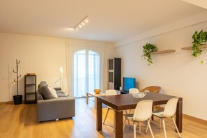 Un salon moderne comprenant un canapé, une table à manger, des chaises, un téléviseur et une plante.