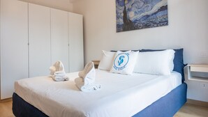 Ett hotellrum med en säng, en tavla på väggen och en kudde med en logotyp.