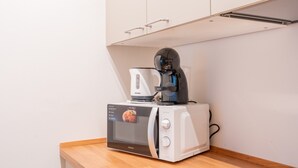 Ett litet kök med en vit mikrovågsugn, en kaffebryggare och en brödrost placerade på en bänkskiva i trä.