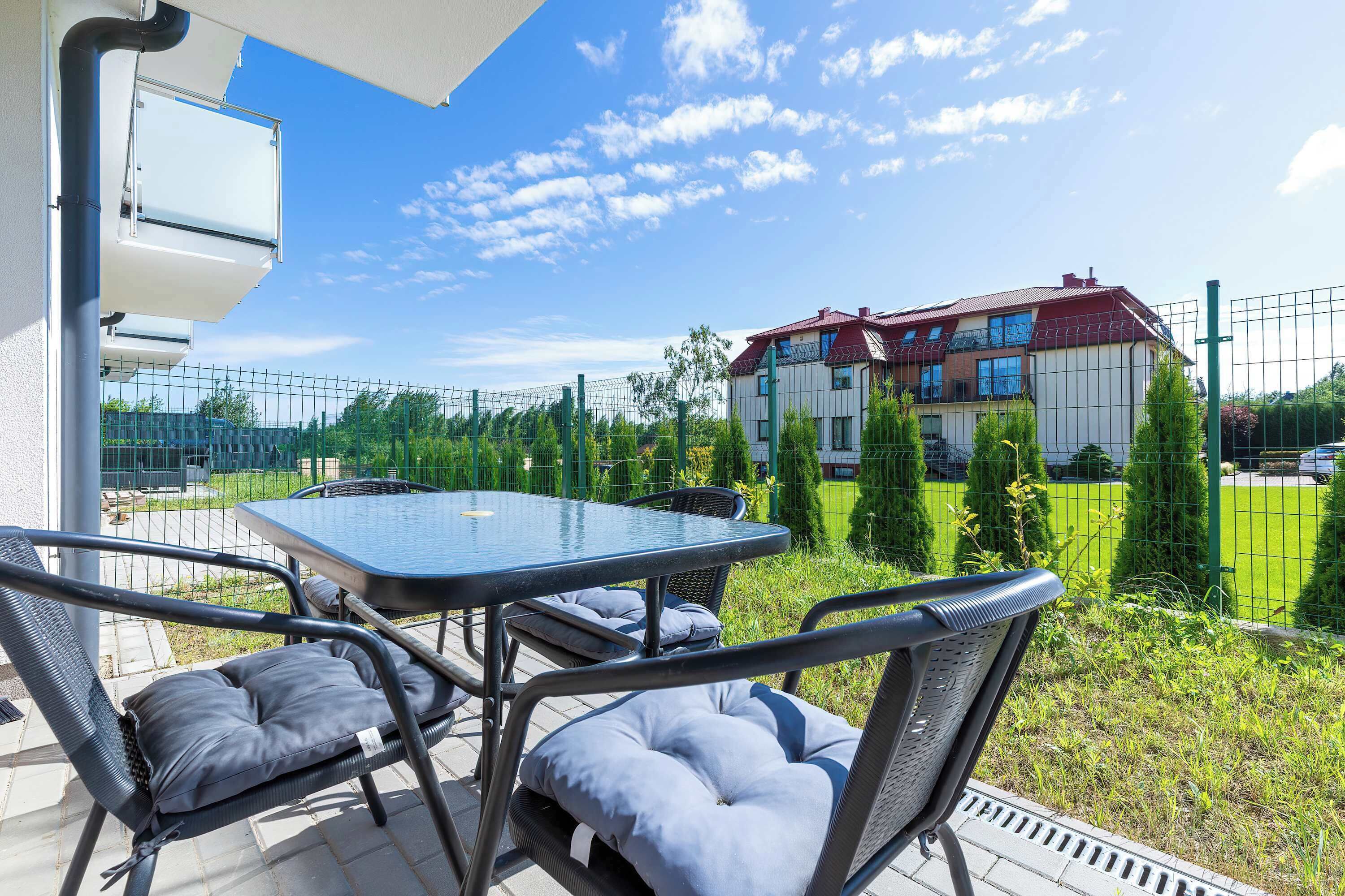 Un patio esterno con tavolo e sedie, vista su un edificio residenziale e una recinzione verde.