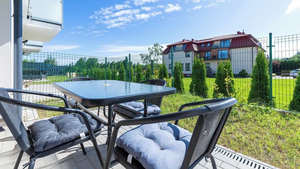 An outdoor patio with a table and chairs, a view of a residential building, and a green fence. - Brown Apartment with Garden | Desk | Parking (Jastrzębia Góra)