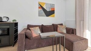 A modern living room with a brown sofa, a glass coffee table, and a kitchen area with a kettle and a microwave. - Brown Apartment with Garden | Desk | Parking (Jastrzębia Góra)