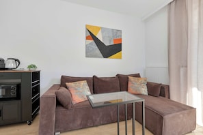 A modern living room with a brown sofa, a glass coffee table, and a kitchen area with a kettle and a microwave. - Brown Apartment with Garden | Desk | Parking (Jastrzębia Góra)