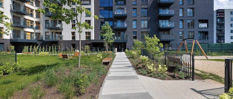 Un moderno edificio de apartamentos con varios balcones, un sendero pavimentado y un jardín ajardinado.