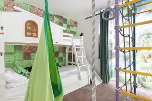 Ein Kinderstockbett mit einem grünen Baldachin, einem weißen Schreibtisch und einem Fenster mit Blick auf Grünflächen.