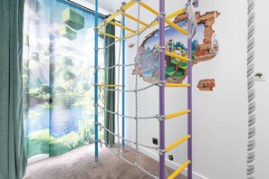 Ein Zimmer mit einer Kletterwand, einem Fenster mit Blick auf ein Gewässer und einer Wand mit einem Minecraft-Wandbild.