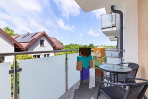 Ein Balkon mit Tisch und Stühlen, Blick auf ein Haus und eine stehende Person.