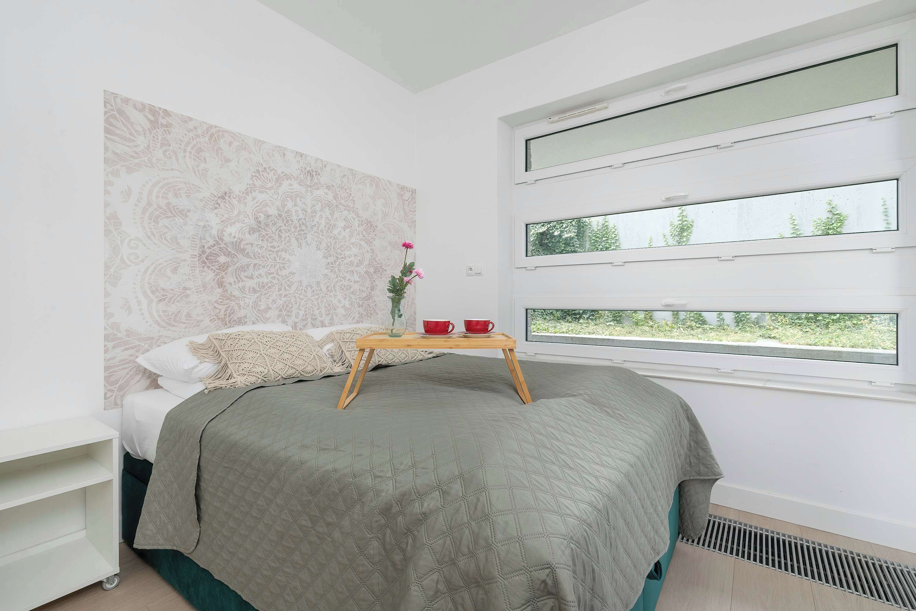 A bedroom with a bed, a bedside table, a window with multiple panes, and a decorative wall piece.