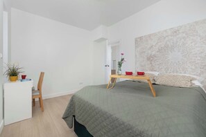 Ein Schlafzimmer mit einem Bett, einem Nachttisch, einem Sessel, einem kleinen Schreibtisch und einer Topfpflanze.