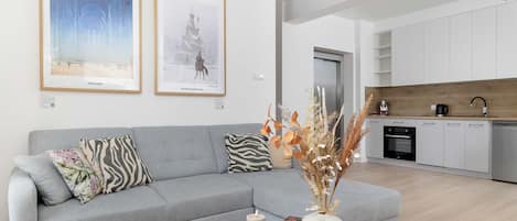A modern living room with a grey sofa, two framed artworks, a vase with dried plants, and a coffee table.