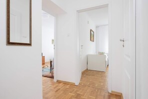 Ein Flur mit Holzboden, weißen Wänden und einer Tür zu einem Zimmer mit Bett und Nachttisch.