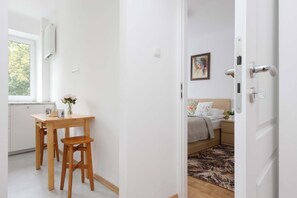 A modern interior with a wooden dining table and chairs, a bed with floral bedding, and a painting on the wall. - Family Apartment for 8 People | Close to the Park (Warszawa)