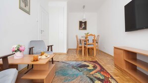 Een gezellig, ruimtelijk interieur met een eethoek, een bank, een aan de muur bevestigde televisie en een kamerbreed tapijt met dessin.