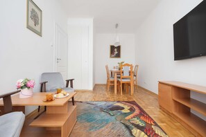 A compact living space with a dining area, a sofa, a TV mounted on the wall, and a patterned rug. - Family Apartment for 8 People | Close to the Park (Warszawa)