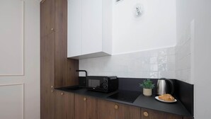 Une cuisine avec un plan de travail noir, un four à micro-ondes, une bouilloire et une plante en pot.