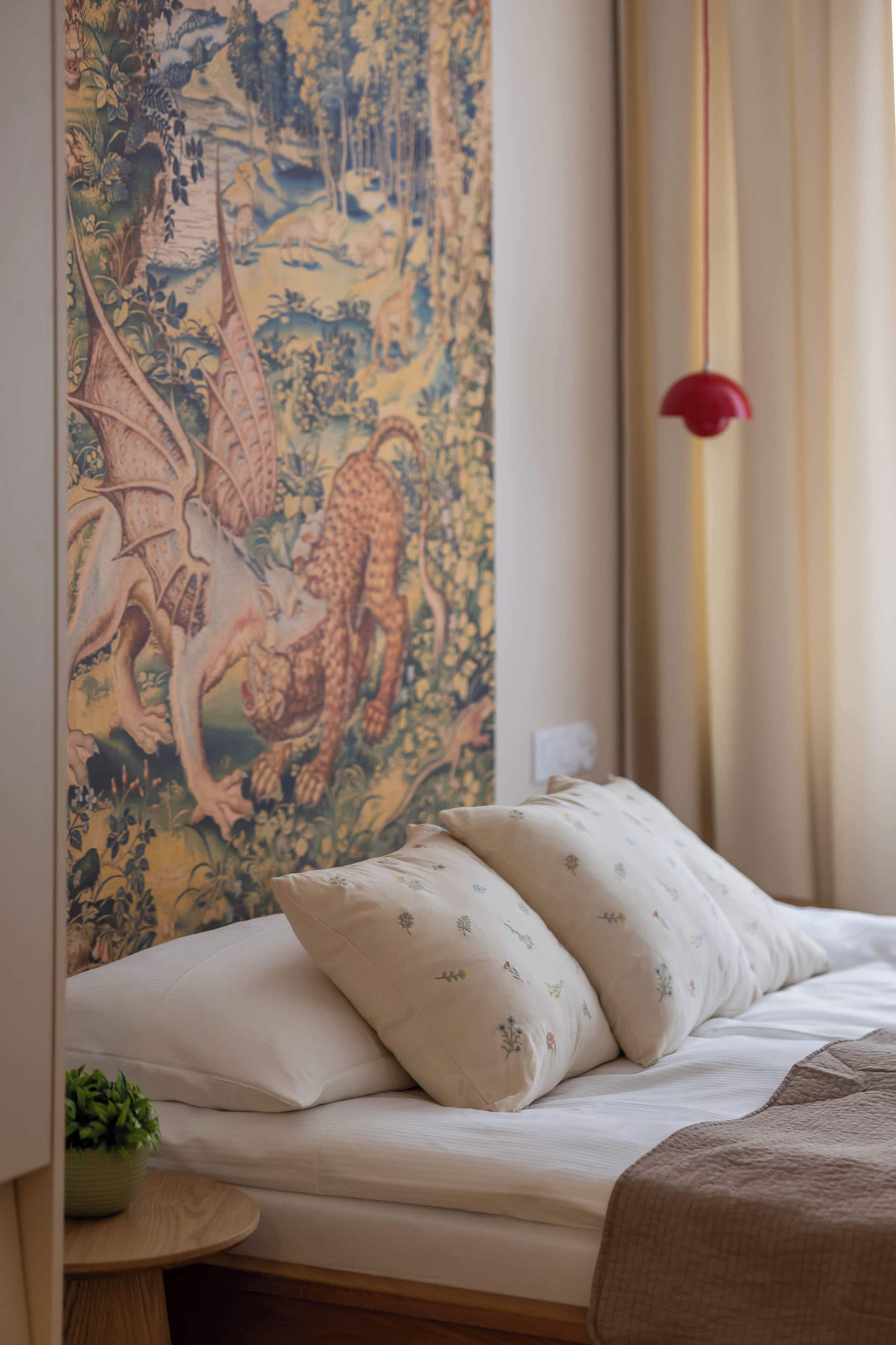 Un letto con biancheria bianca e cuscini decorativi, un arazzo con un motivo a drago sulla parete e una lampada pendente rossa.