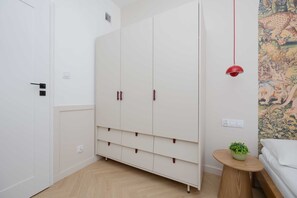 A bedroom with a bed, a small round wooden table with a plant, a white wardrobe with two doors, and a red pendant light. - Elegant Apartment in Center | By the Market (Warszawa)