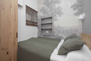 Ein Schlafzimmer mit einem Bett, einem Fenster mit Jalousien, einem Wandregal und einer Wandleuchte.