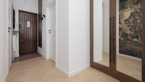 Un couloir avec une porte en bois, un mur blanc et une porte dotée d’un miroir qui reflète un tableau.