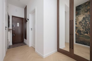 Ein Korridor mit einer Holztür, einer weißen Wand und einer Tür, in deren Spiegel ein Gemälde zu sehen ist.