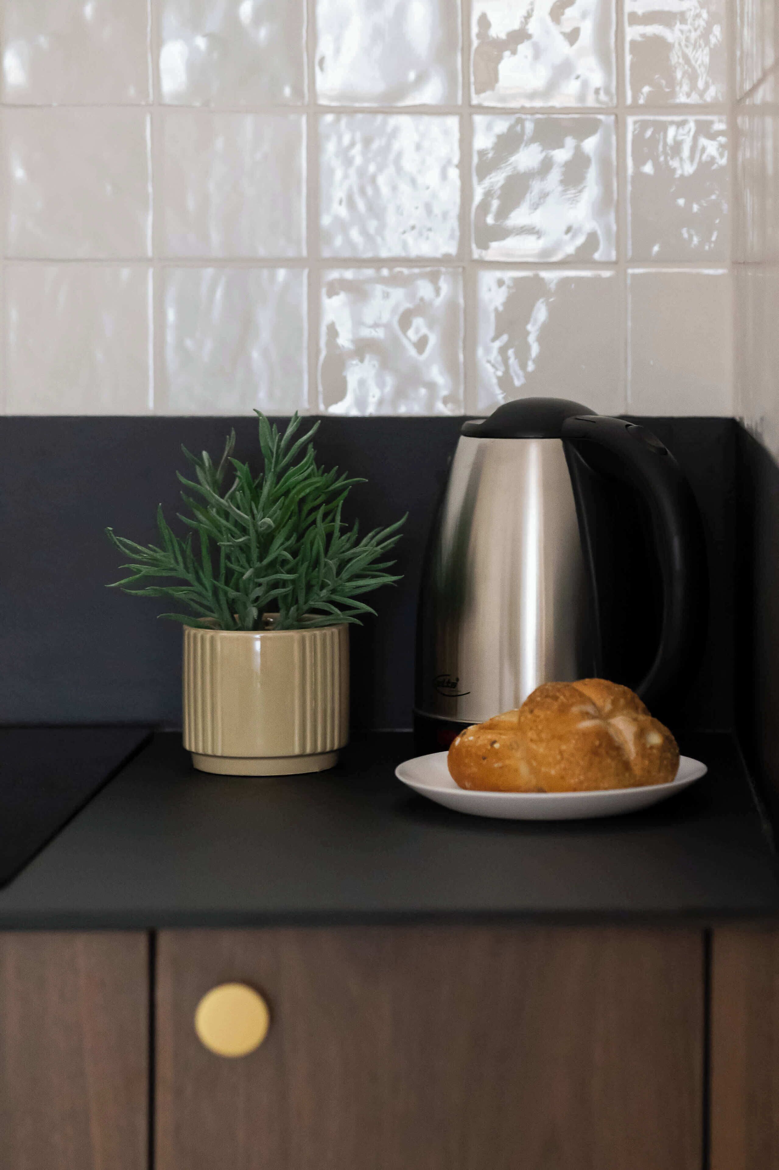 A kitchen counter with a potted plant, a coffee maker, and a plate with a pastry.