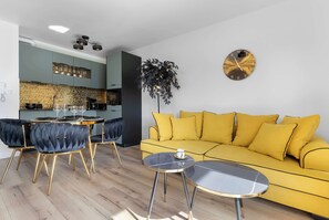 Ein modernes Wohnzimmer mit einem gelben Sofa, einem runden Couchtisch und einem Essbereich mit einem Glastisch und Stühlen.