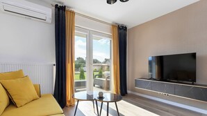 Un salon moderne comprenant un canapé, une table à plateau en verre, un téléviseur à écran plat et une porte-fenêtre coulissante donnant sur un espace extérieur.