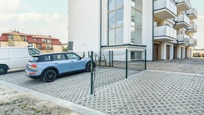 Un bâtiment moderne doté d’un espace de stationnement, d’une voiture bleue et d’un fourgon blanc.