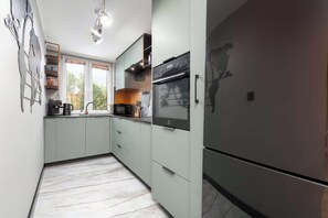 A kitchen with a built-in oven, a refrigerator, and a window with blinds. - Mosaic Apartment with Air Conditioning | Center (Rzeszów)