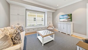 A living room with a sofa, a coffee table, a TV, and a window with blinds. - New Oceanfront Jekyll Home • Beach Boardwalk • Fireplace Porch (Jekyll Island)